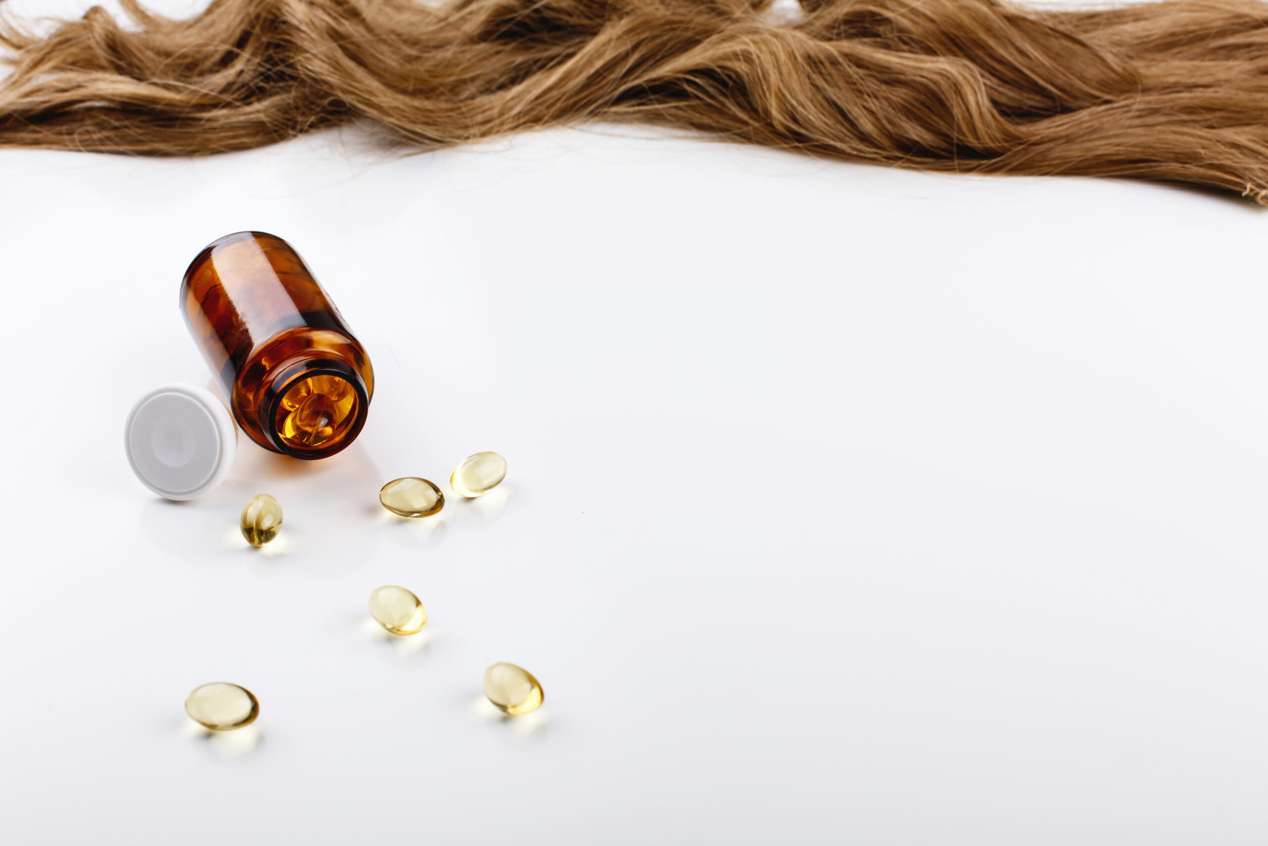 Bottle with vitamins lies before brown hair curl